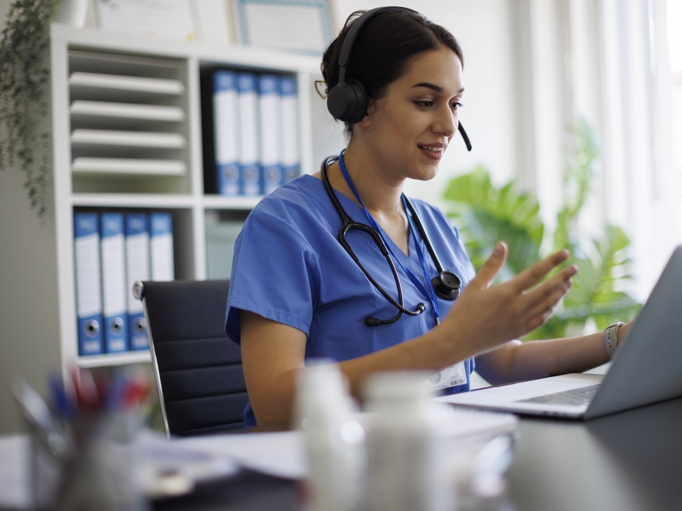 A specialist wearing a headset, consulting by video call from a clinic workstation.